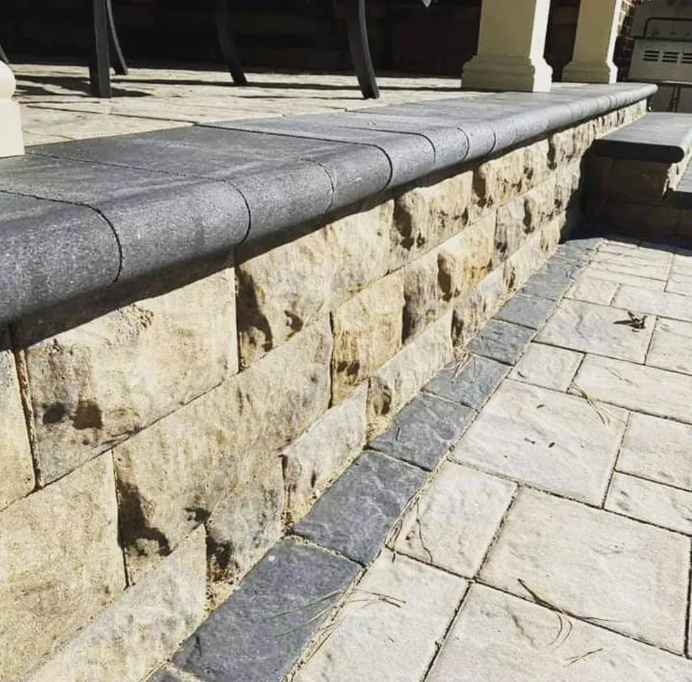 A stone wall is surrounded by bricks on a patio.