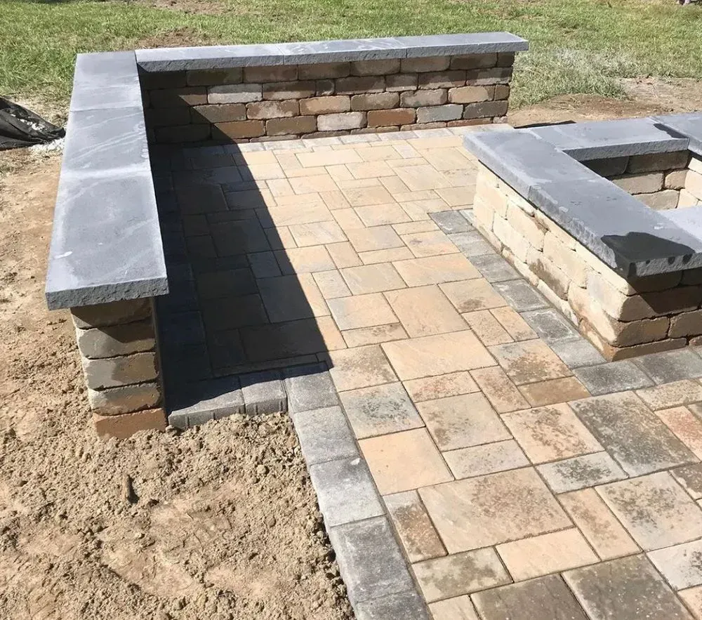 A brick patio with a fire pit and a bench.