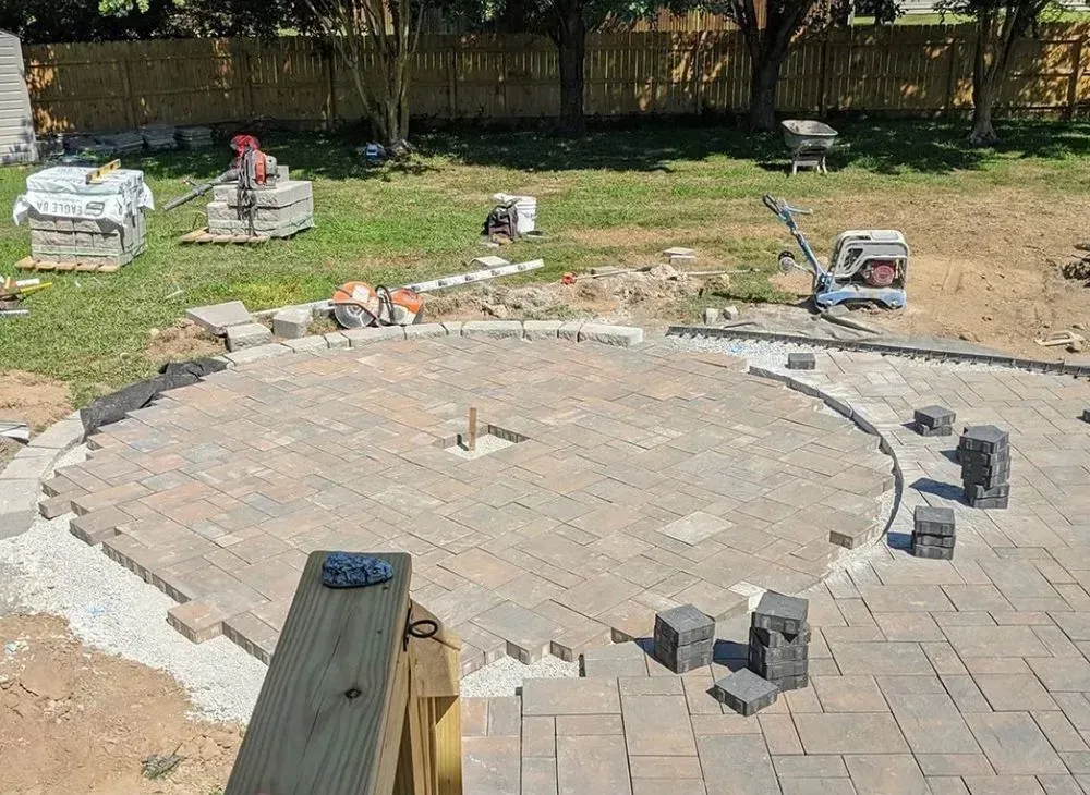 A brick patio is being built in a backyard.