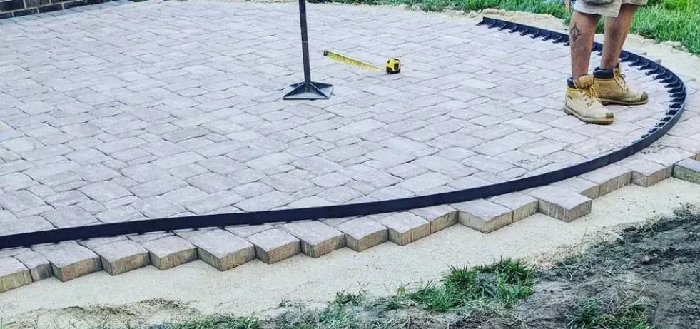 A man is measuring a brick patio with a tape measure.
