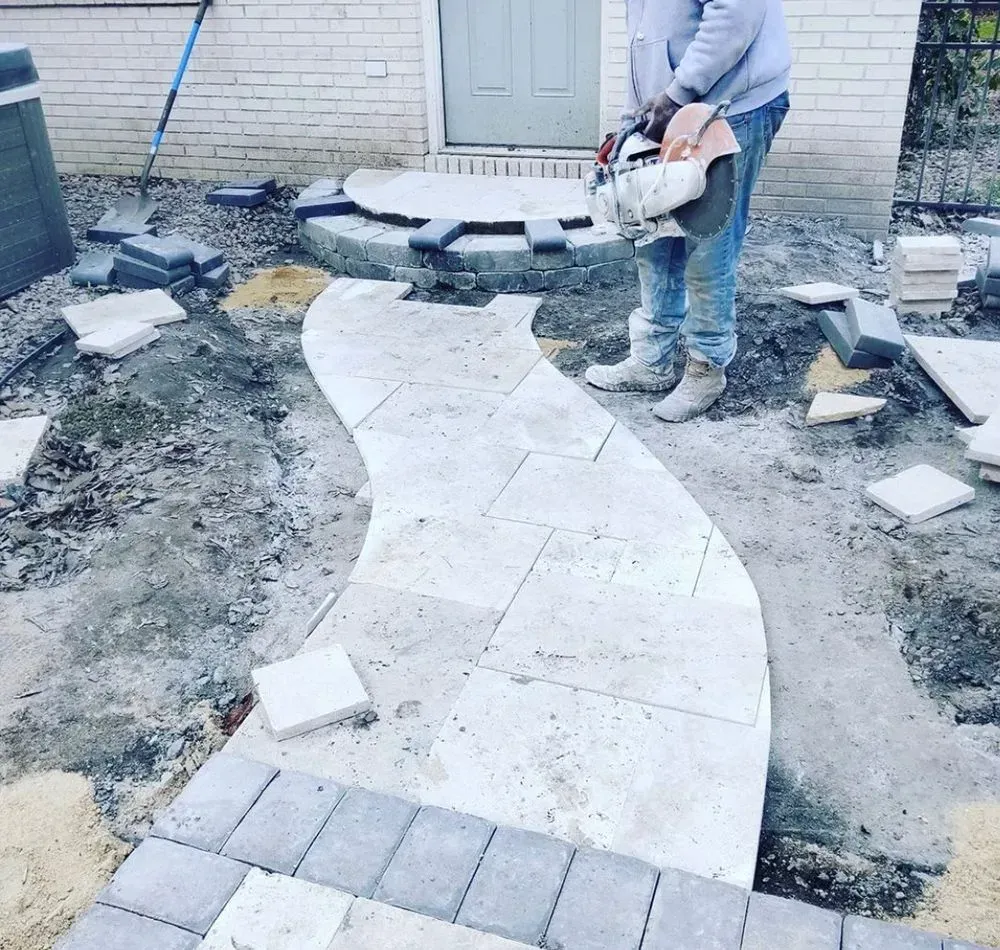 A man is laying bricks on a walkway in front of a house.