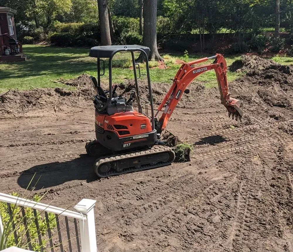 A small orange excavator is digging in the dirt in a yard.