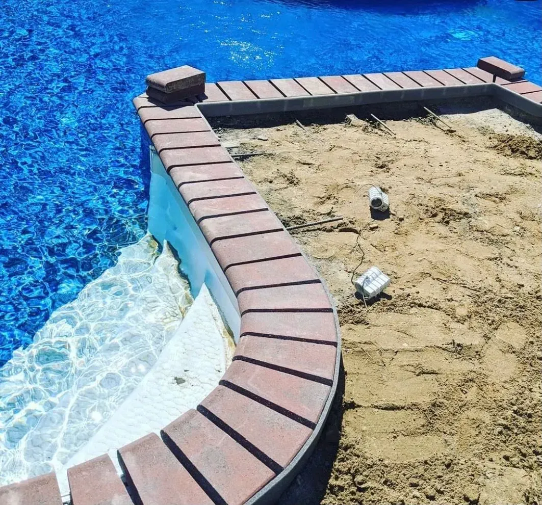 A brick walkway is being built next to a swimming pool