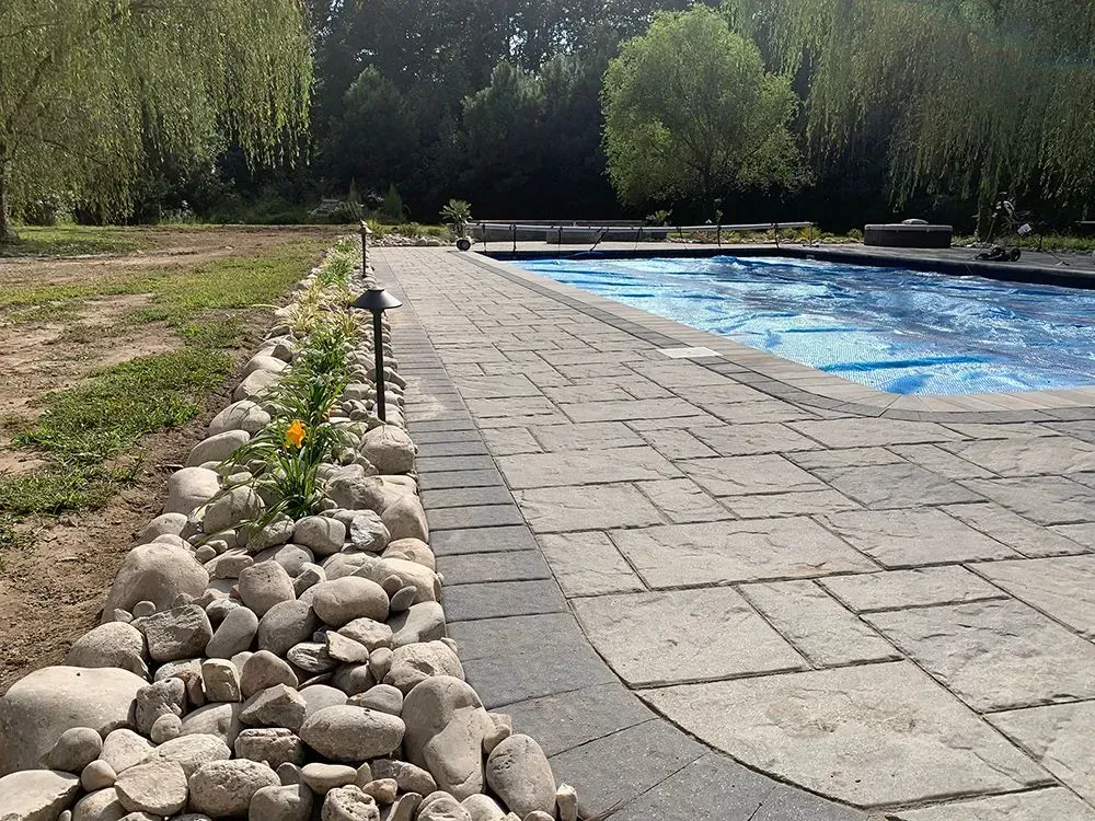 A brick walkway leading to a large swimming pool surrounded by rocks.