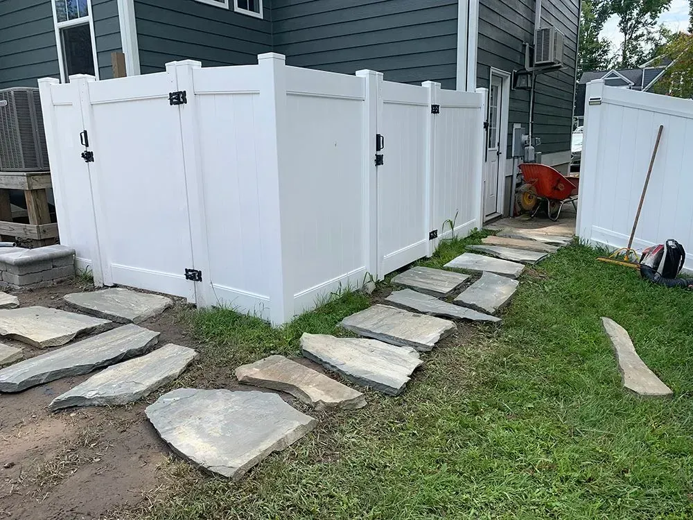 A white fence with a stone walkway leading to a house.