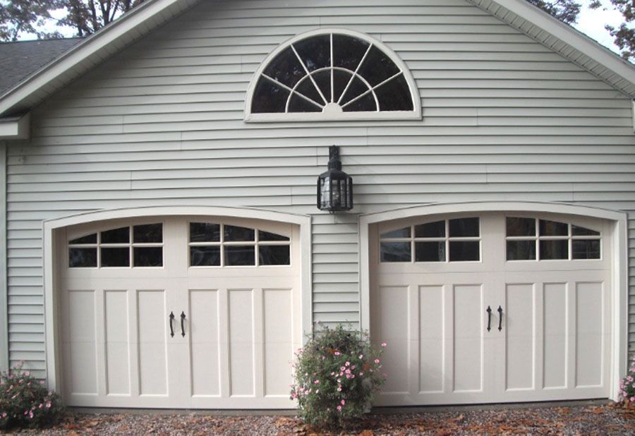 Two white garage doors with arched windows on a house