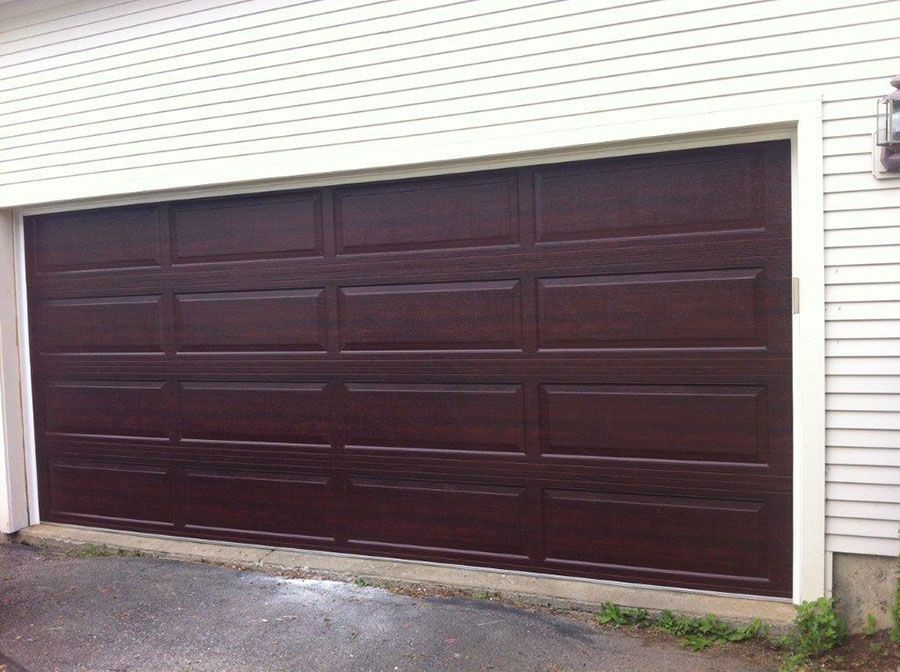 A brown garage door is sitting in front of a white house
