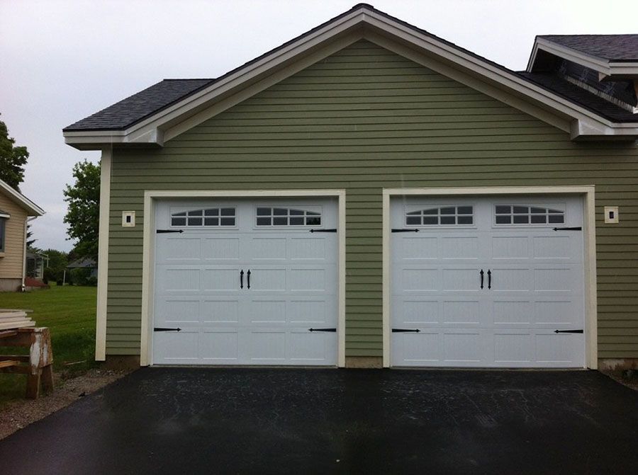 A green house with two white garage doors