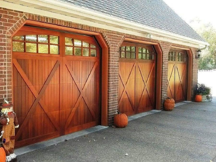 Three wooden garage doors are lined up in front of a brick building