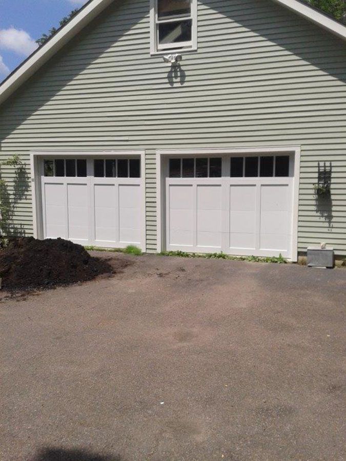 A green house with two white garage doors