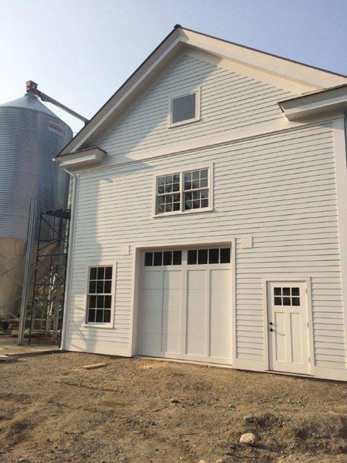 A white barn with a silo in the background