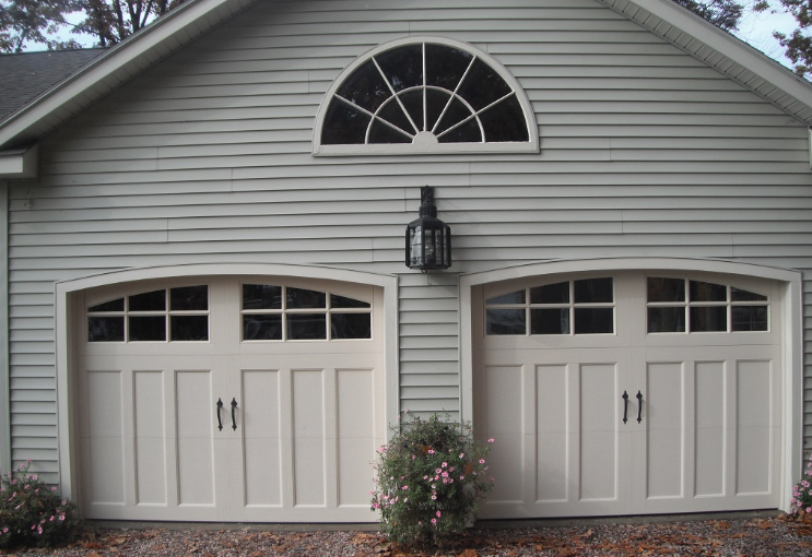 Two white garage doors with arched windows on a house