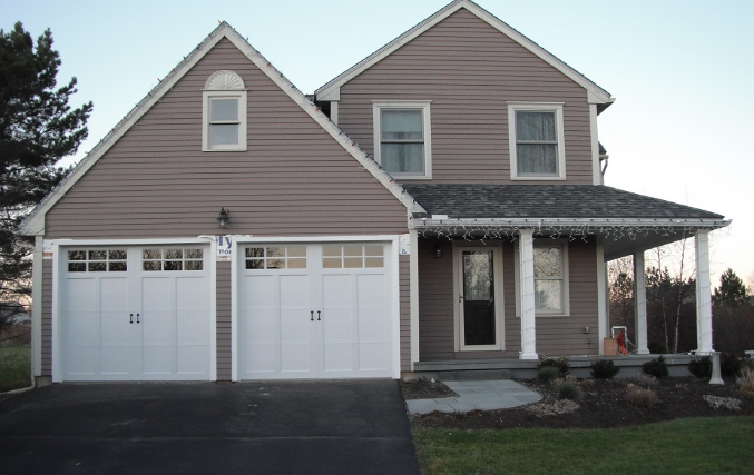 A brown house with white garage doors and a porch