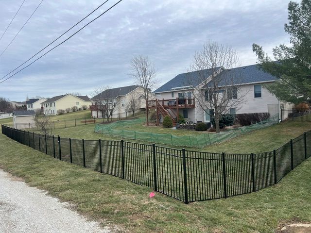Backyard fenced with black metal panels beside suburban houses on a cloudy day