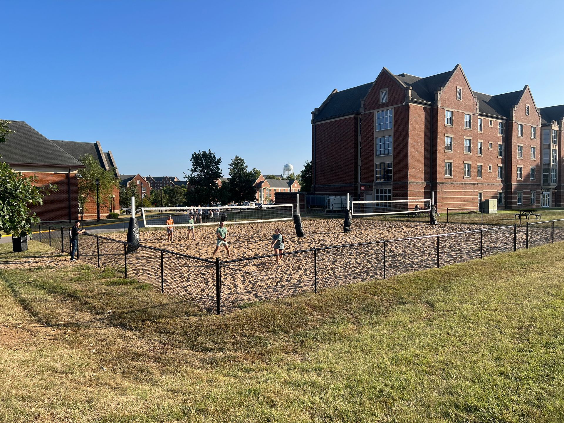 Brick apartment buildings beside a fenced gravel lot under a clear blue sky