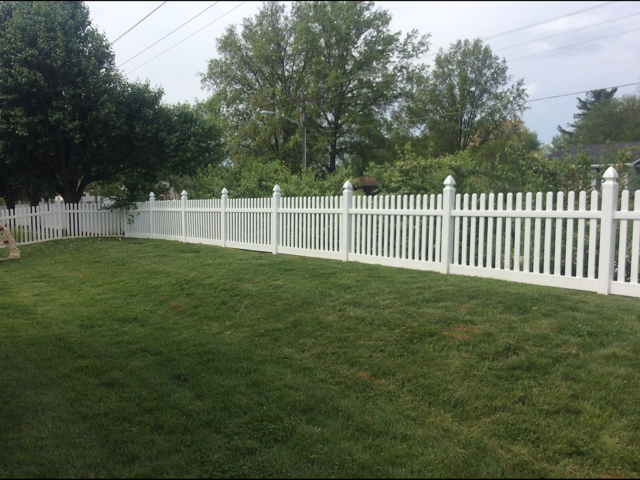White picket fence along a green lawn under cloudy sky