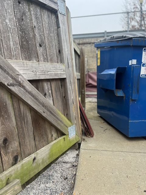 Chain-link fence beside the blue dumpster on a concrete alleyway