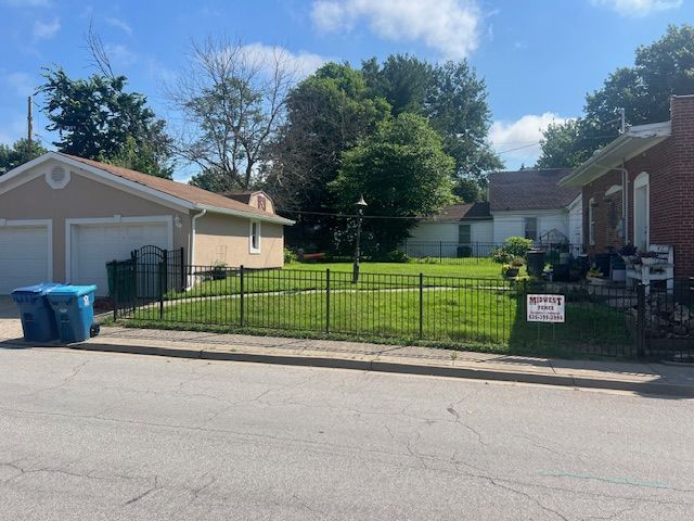 Residential yard with black metal fence, blue bins, and a “No Trespassing” sign beside a driveway