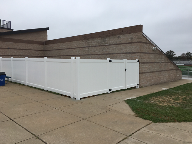 White vinyl fence enclosing a concrete area beside a brick building under an overcast sky