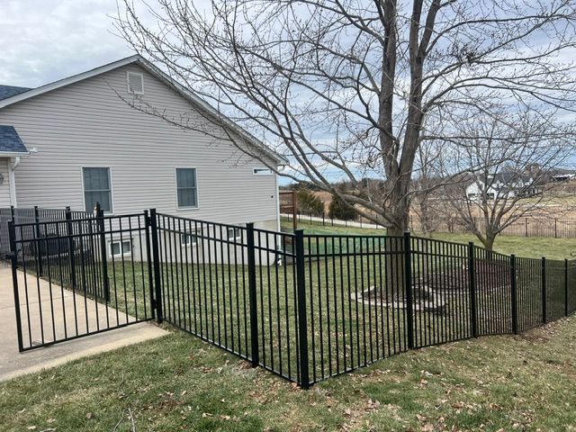 Black metal fence enclosing a sloped backyard beside a beige house under leafless trees