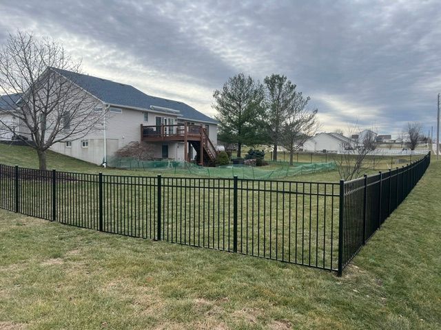 Black metal fence around a grassy backyard with a house and cloudy sky in the background