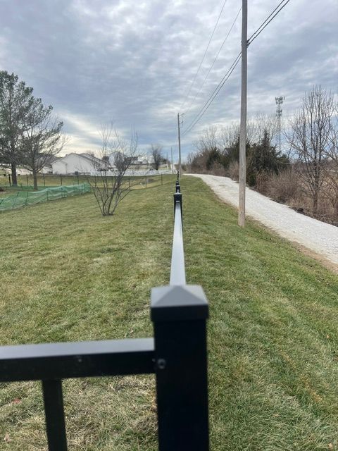 Black fence and grassy path beside a paved trail under a cloudy sky, with utility poles along the road