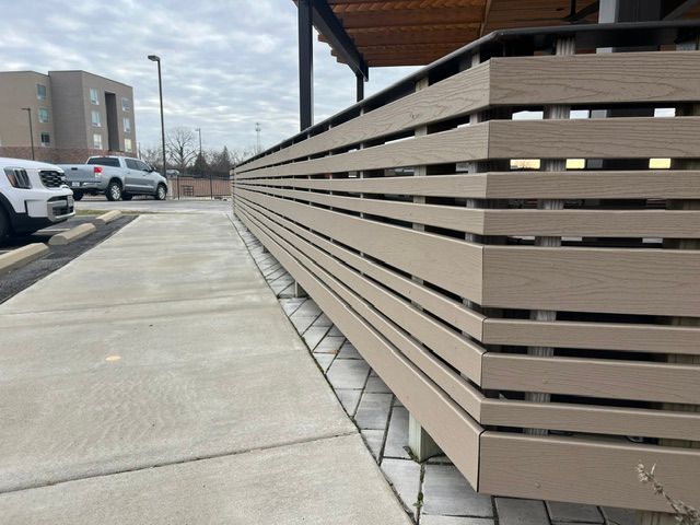 Long beige slatted fence beside a concrete sidewalk outside a building on an overcast day