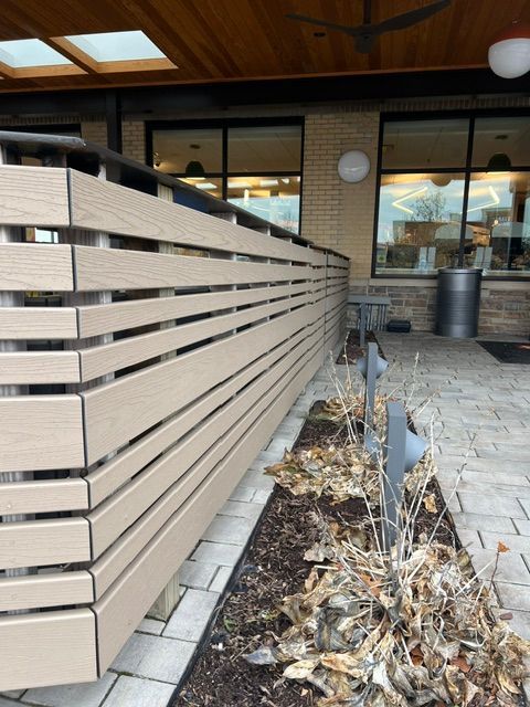 Modern outdoor patio with wooden slat fencing, potted plants, and a brick walkway outside a building