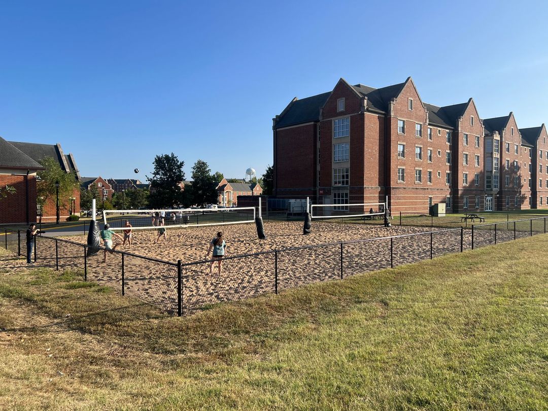 Apartment building beside fenced gravel lot with a child and dog under a clear blue sky