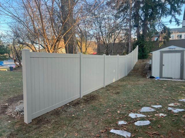 Light gray privacy fence curving through a backyard beside a small shed and trees