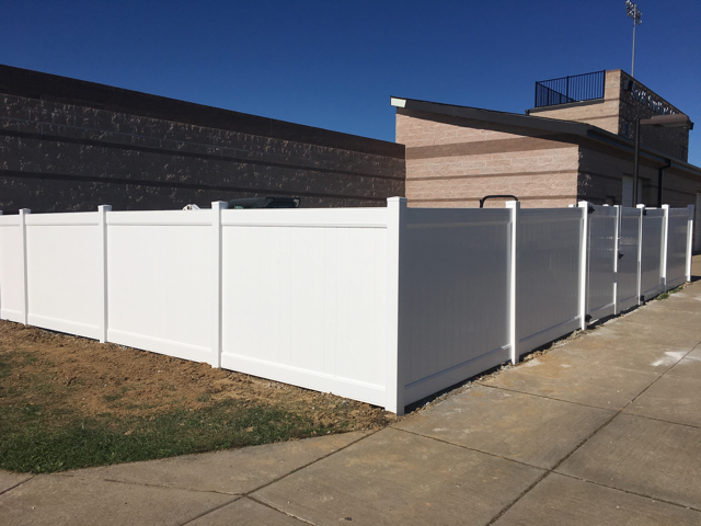 White vinyl fence beside a sidewalk and building in bright sunlight