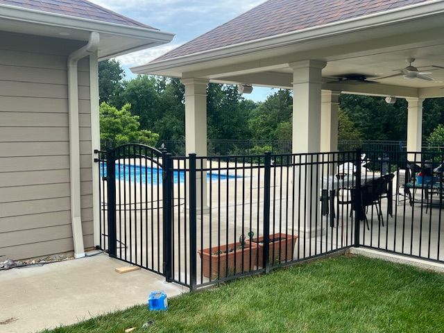 Backyard patio with black metal fence, pool, and covered seating area beside a house.