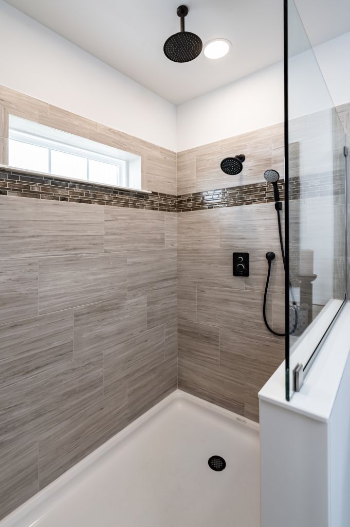 Modern shower with tan tile, black fixtures, glass door, and white base.