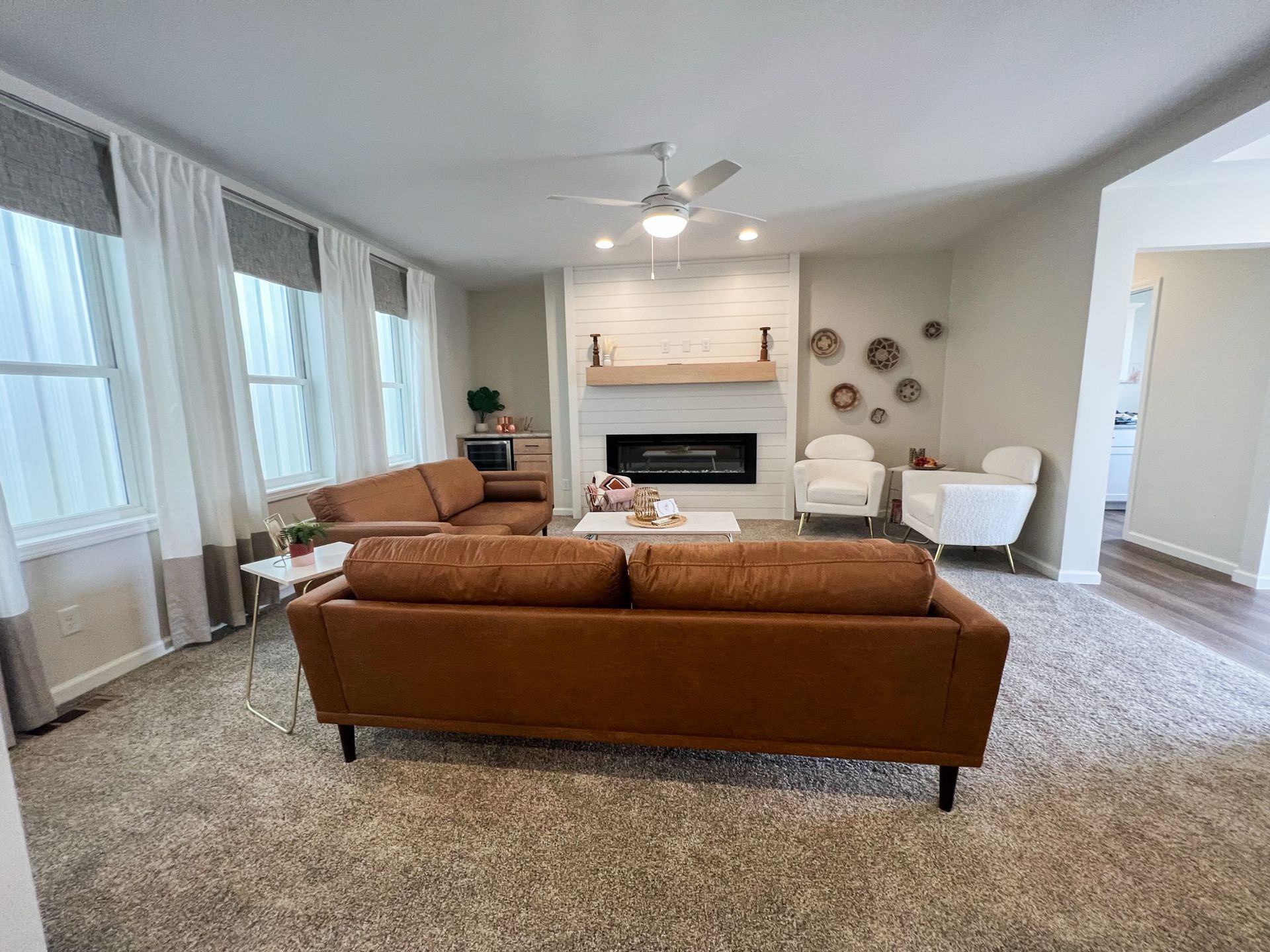 A modern living room with brown leather sofas, a fireplace, and white curtains.