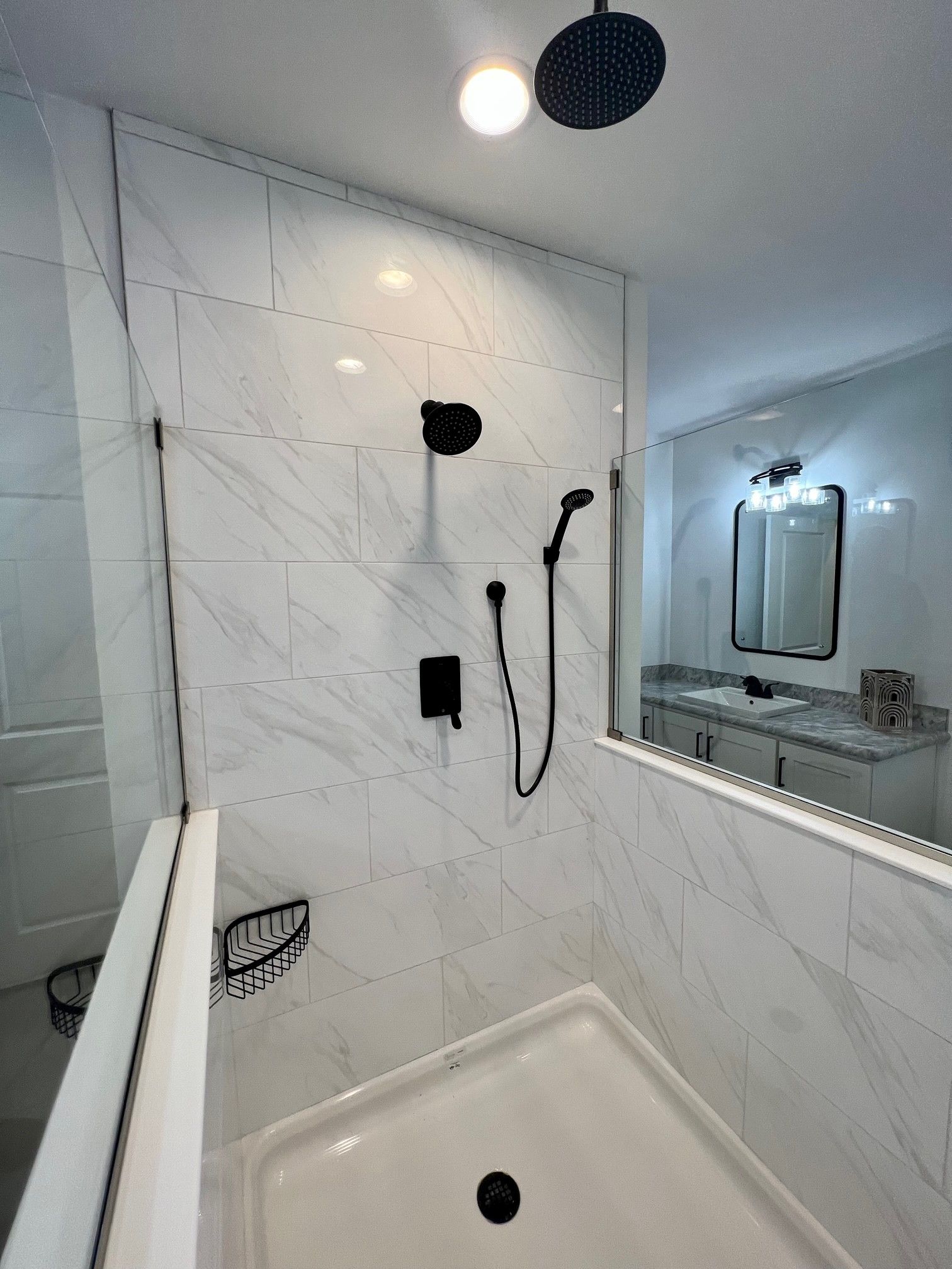 Modern white tiled shower with black fixtures and a separate vanity area.