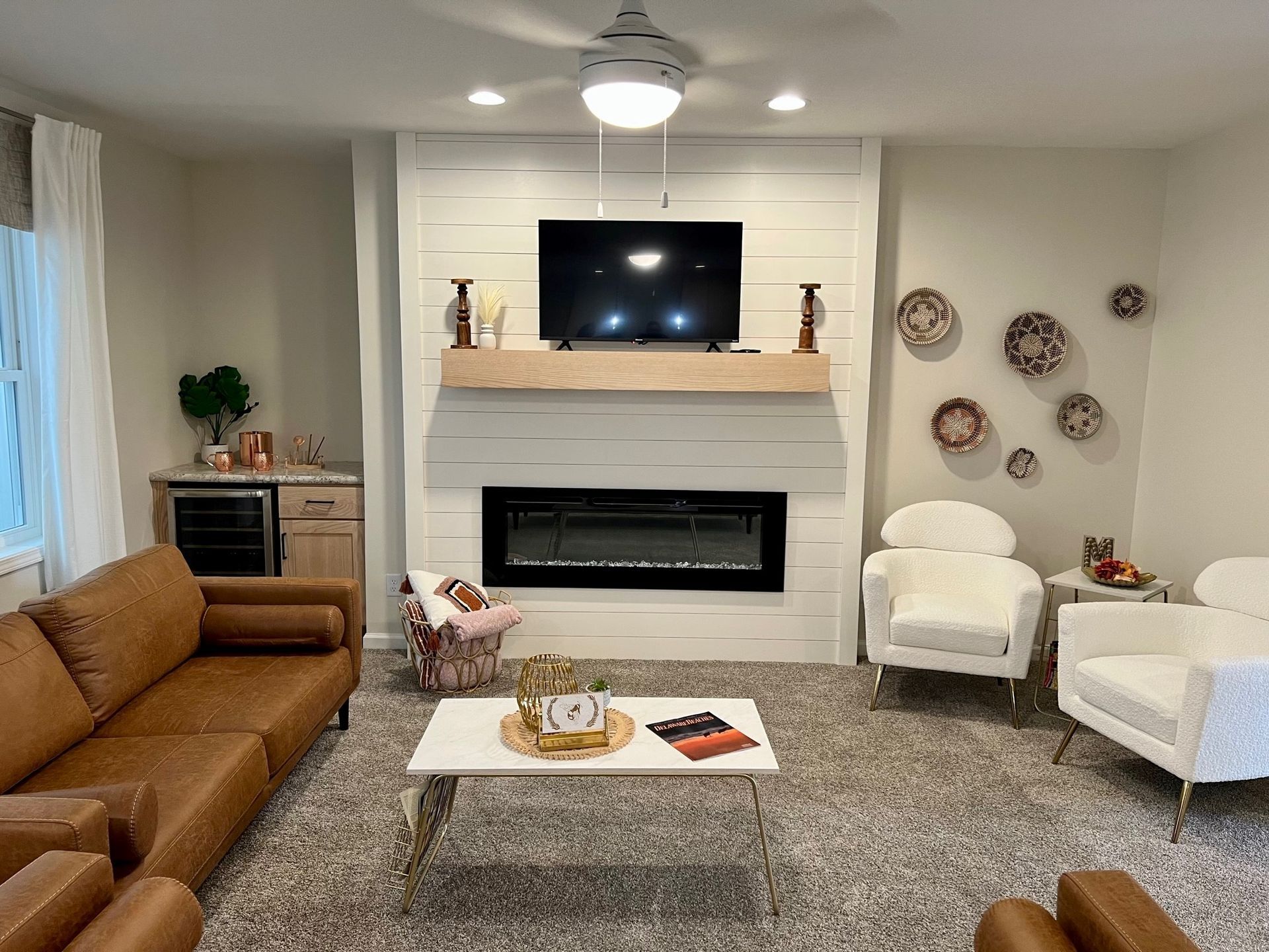 Living room with fireplace, TV, white and brown decor, leather couch and white chairs.