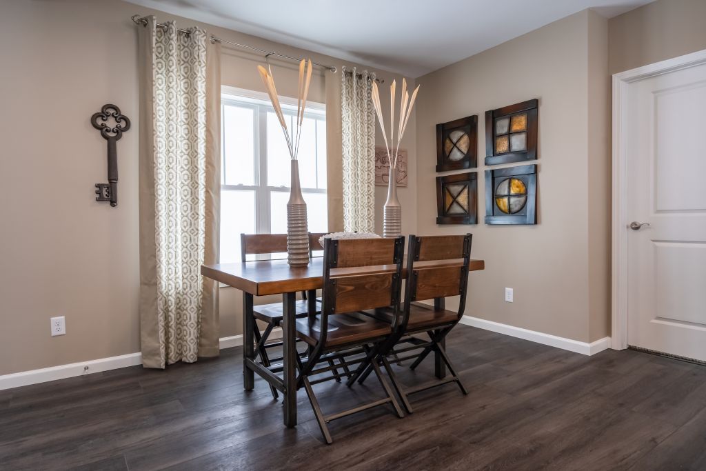 Dining room: wooden table and chairs, window with beige curtains, decorative wall art, and dark wood floor.