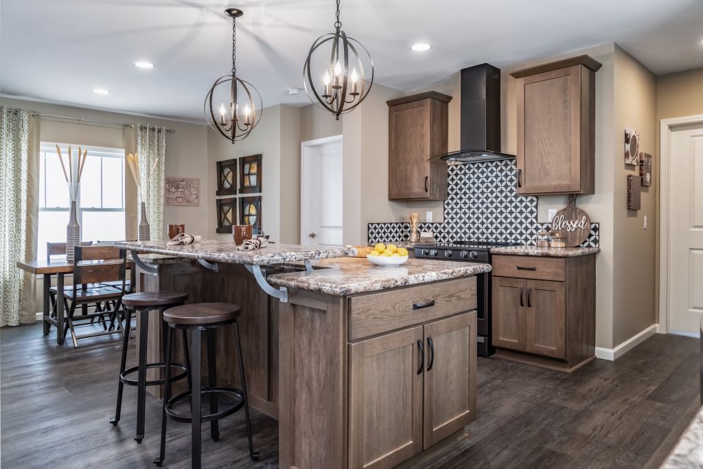 Spacious kitchen with island, brown cabinetry, granite countertops, and pendant lights.