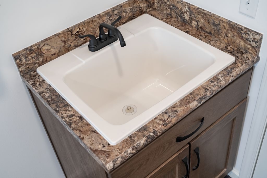 White utility sink with black faucet on a brown countertop and a dark brown cabinet.