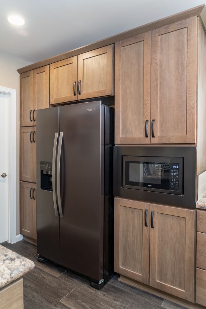 Kitchen cabinets with a dark refrigerator and built-in microwave. Light wood cabinets and dark floor.