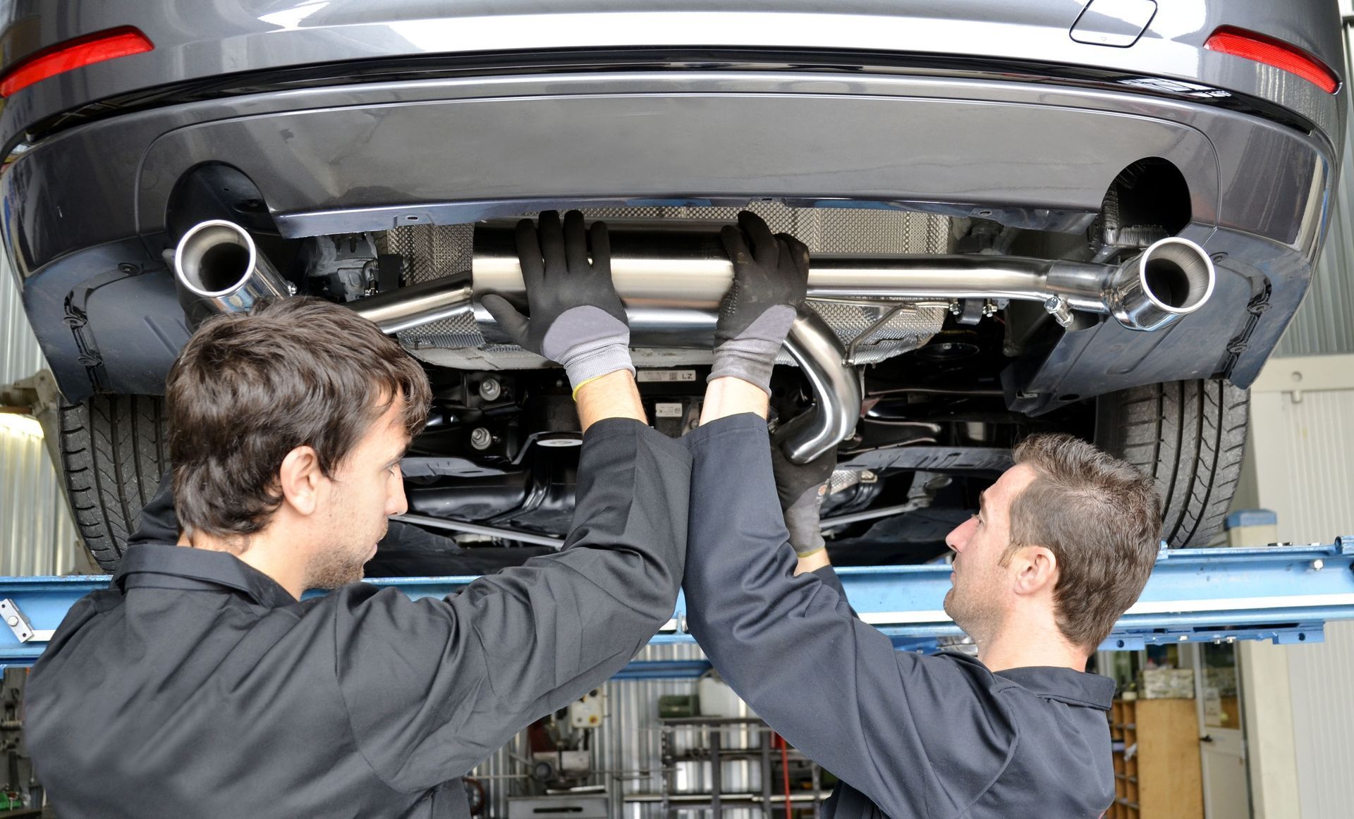 Two mechanics installing an exhaust system under a car raised on a lift.