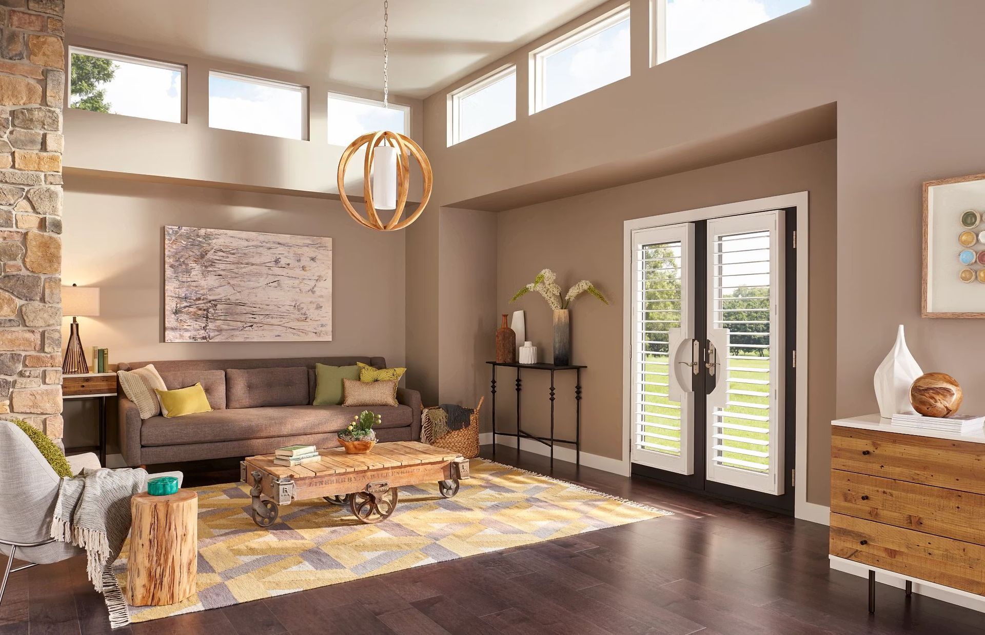 Modern living room with brown sofa, colorful rug, coffee table, and French doors letting in bright light