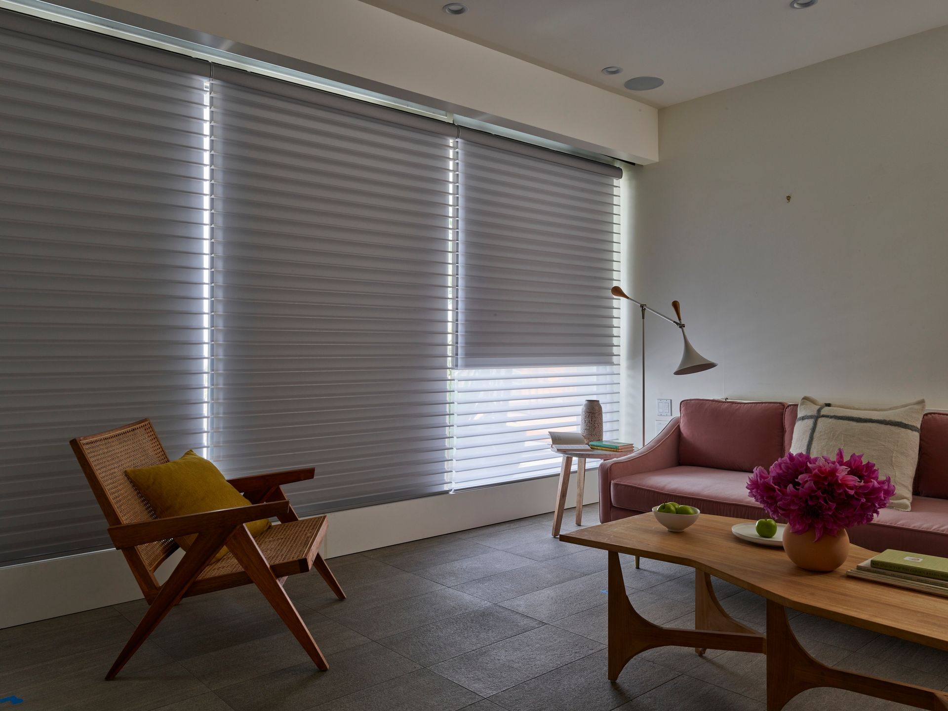Minimalist living room with blinds, wooden lounge chair, pink sofa, and coffee table with flowers