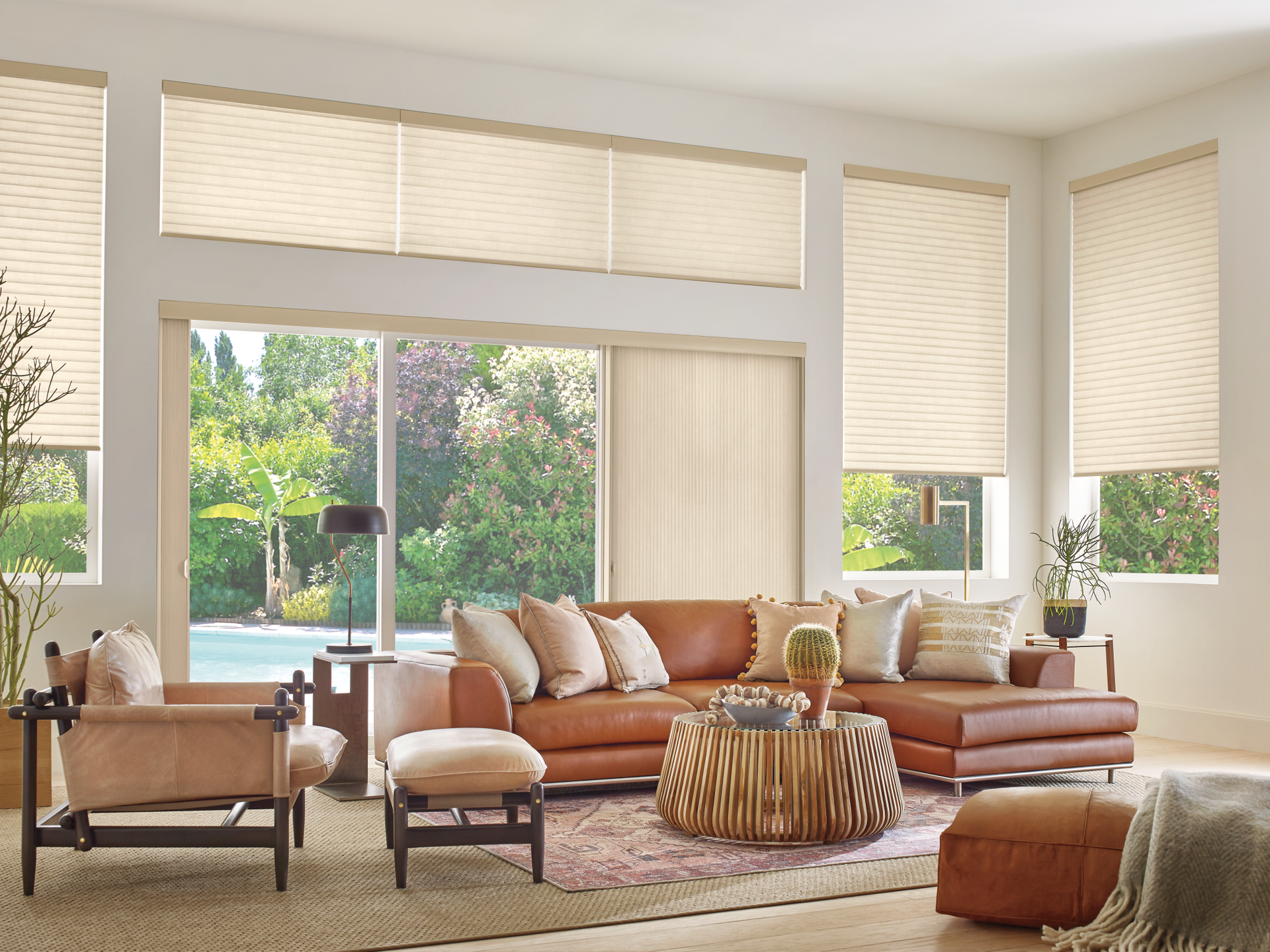 Bright living room with tan sofa, armchairs, and large windows overlooking a green garden.