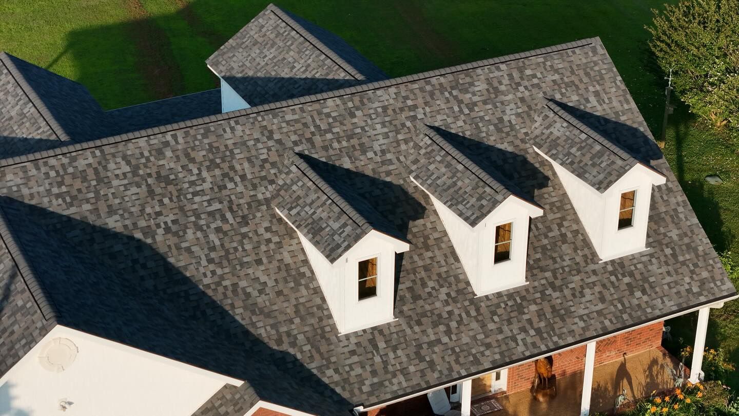 An aerial view of a house roof with gray shingles and three dormer windows.