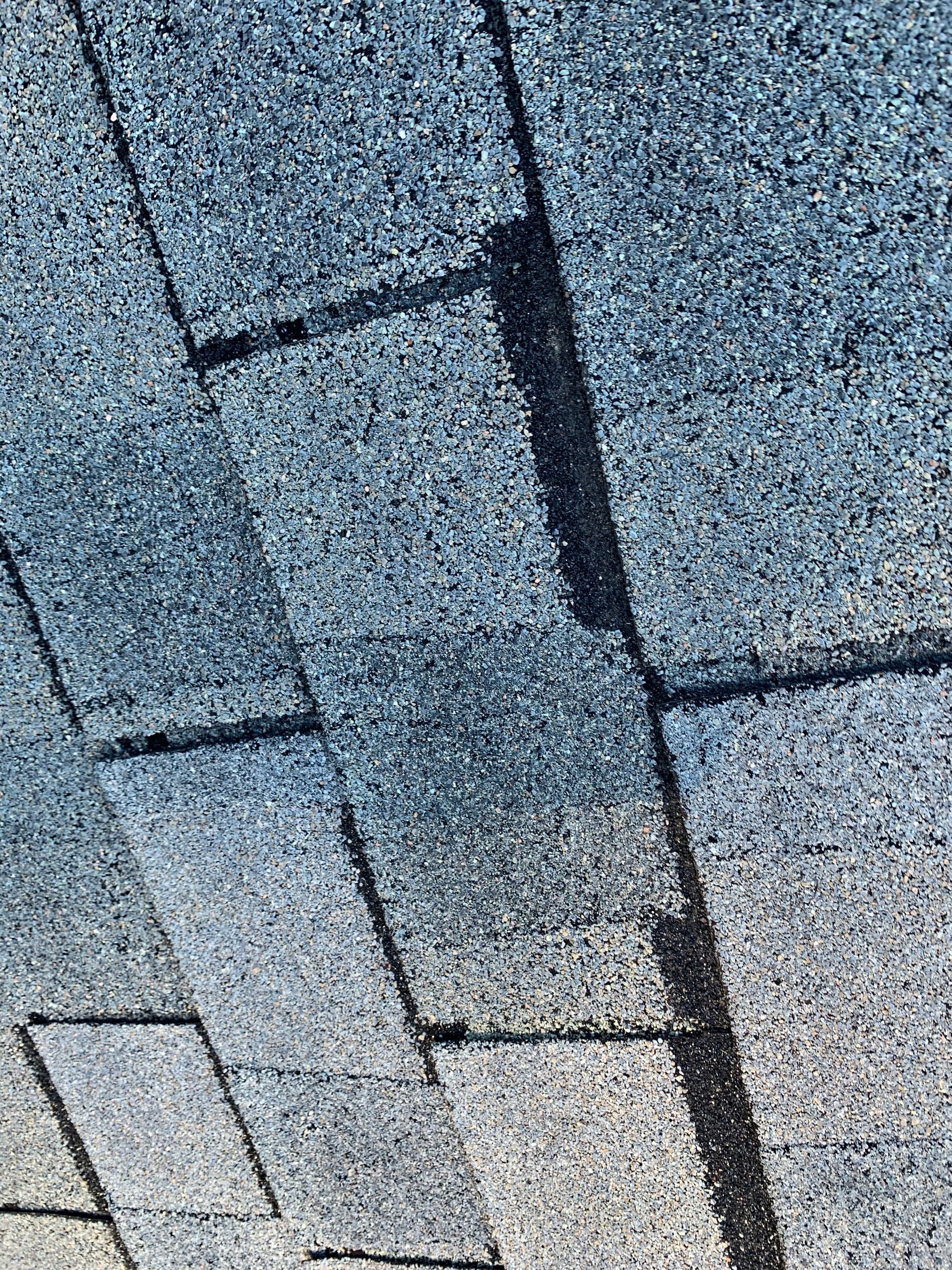 Close-up view of overlapping grey, textured asphalt roof shingles in a staggered pattern.