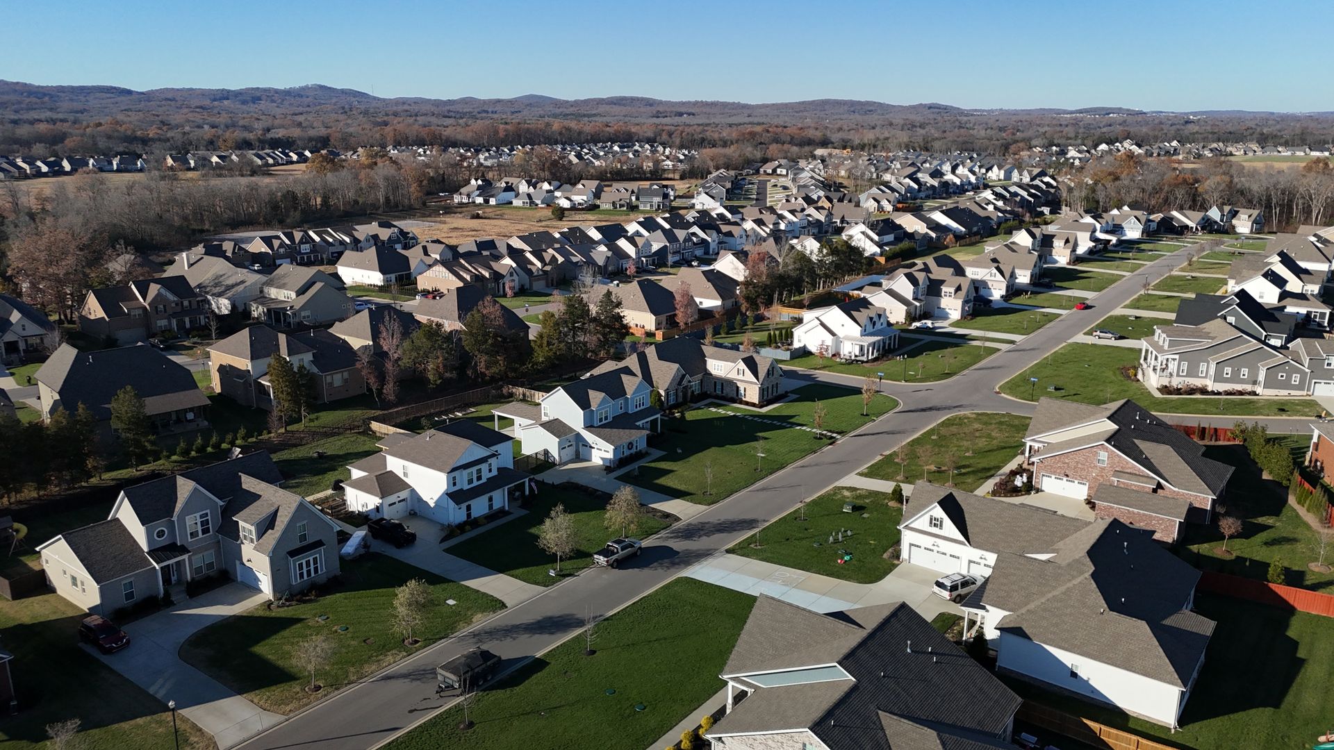 Aerial view of a residential suburban neighborhood featuring detached houses, green lawns, and winding roads.