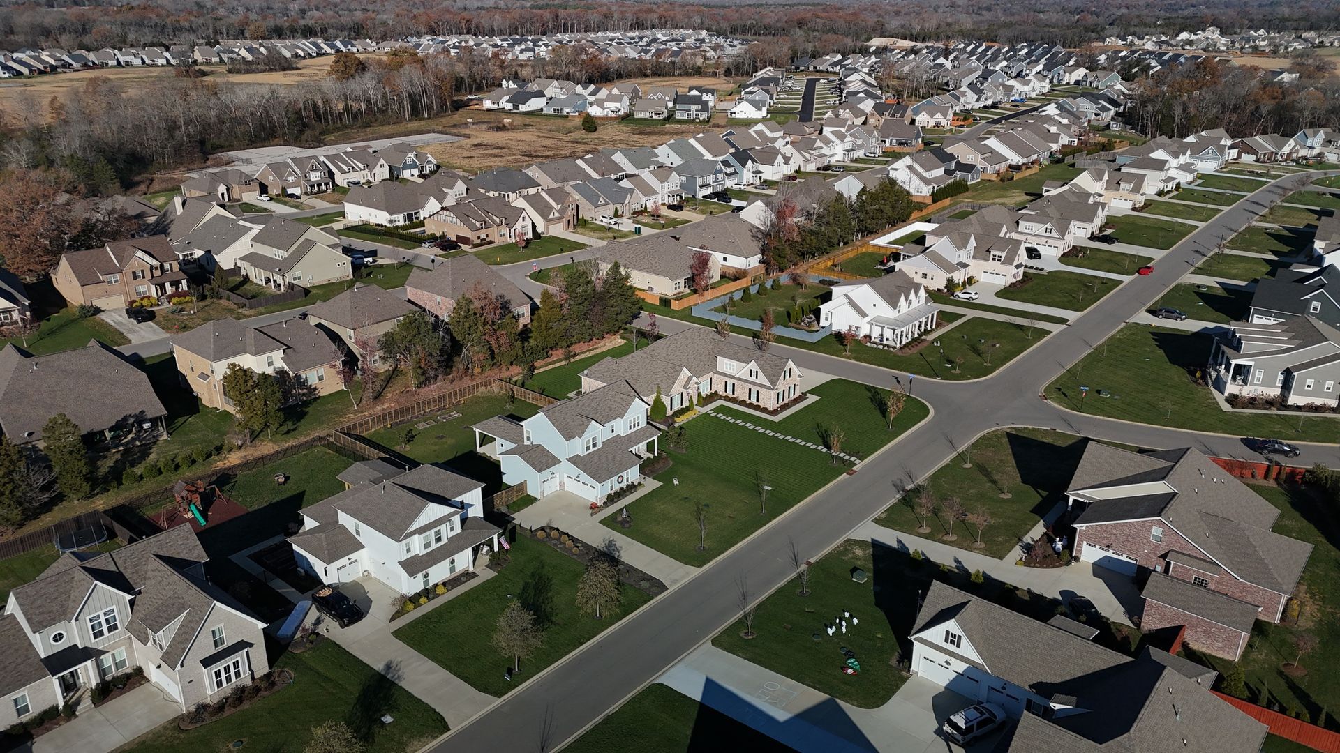 An aerial view of a suburban neighborhood with many detached houses, green lawns, and intersecting paved streets.