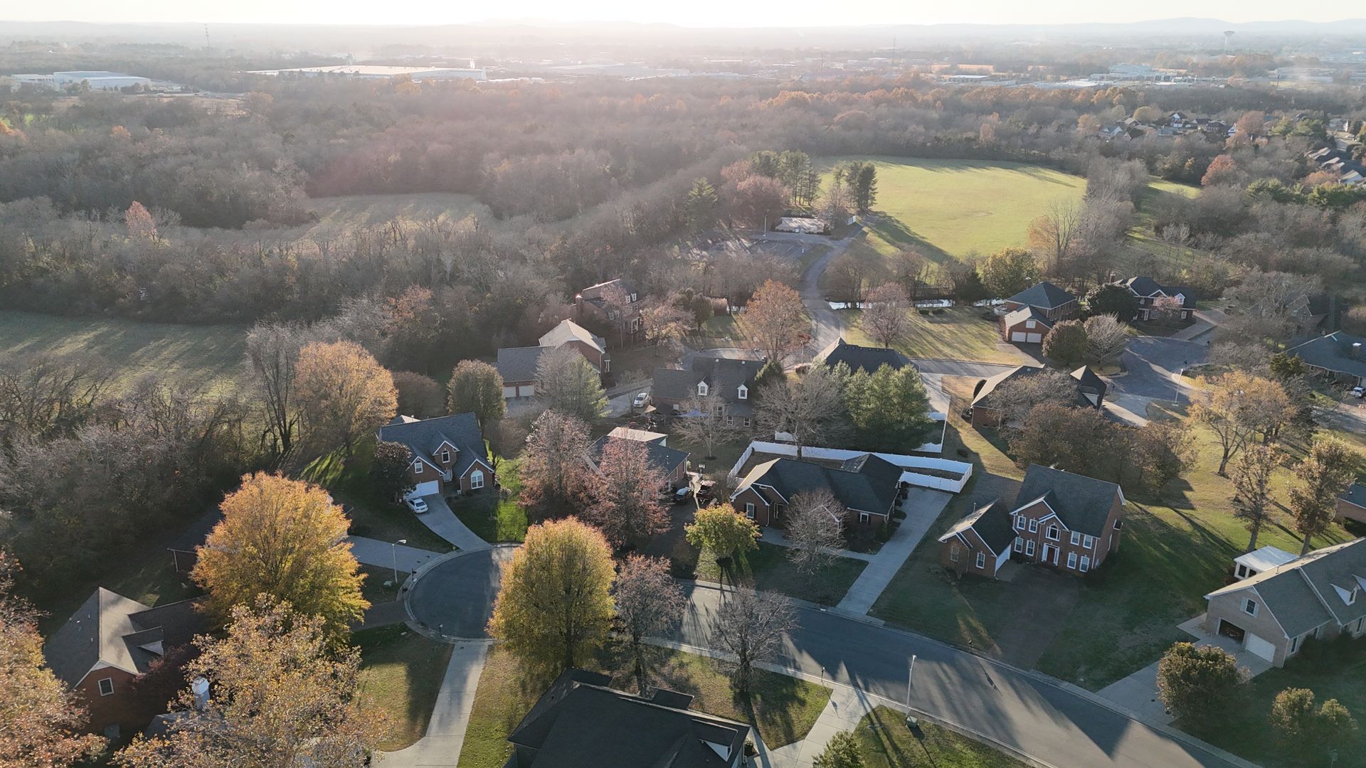 An aerial view of a suburban neighborhood with houses surrounded by trees and a nearby field during autumn.