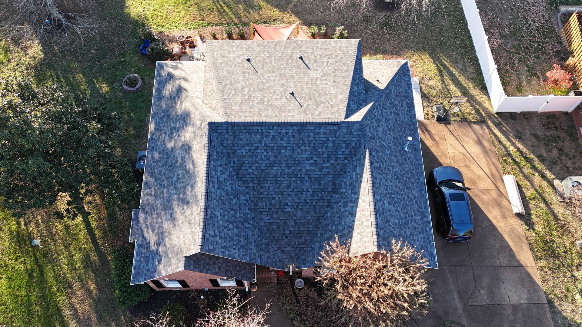 Aerial view of a gray shingled roof on a house with a driveway and car in a residential neighborhood.